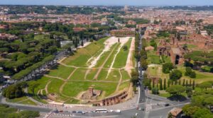 L'immagine mostra una vista aerea del Circo Massimo a Roma, l'antico stadio romano situato nella valle tra il colle Palatino (visibile sul lato destro) e l'Aventino.