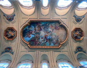 The image shows the ceiling of the central nave of the Basilica of Santa Cecilia in Trastevere in Rome. At the center is the large fresco depicting the Coronation of Saint Cecilia in Heaven, painted in 1727 by the Baroque painter Sebastiano Conca.